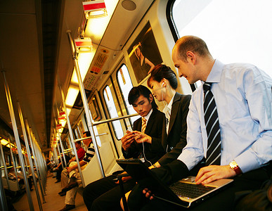 听歌看书商务摄影照片_上海城铁车厢内三位中外商务人士使用笔记本电脑和MP3