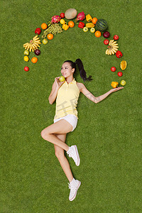 年轻女子手托着水果躺在草地上