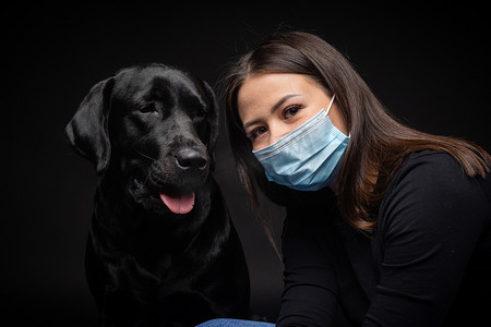 一个拉布拉多猎犬的肖像，带着一个保护的医疗面具和一个女主人在一起。这张照片是在摄影棚拍的