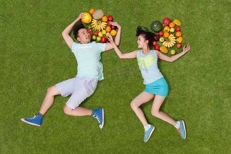 青年男女拿着水果躺在草地上