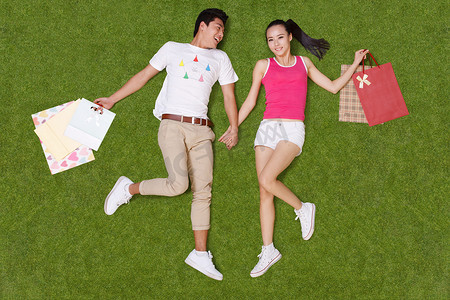青年男女手提购物袋躺在草地上
