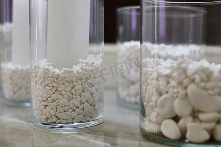 玻璃瓶装饰摄影照片_漂亮的室内装饰，用白色的石头装饰在大理石桌上的透明玻璃瓶中.