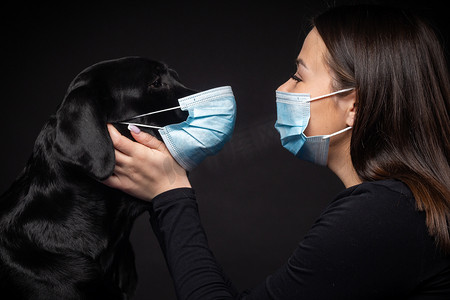 一个拉布拉多猎犬的肖像，带着一个保护的医疗面具和一个女主人在一起。这张照片是在摄影棚拍的