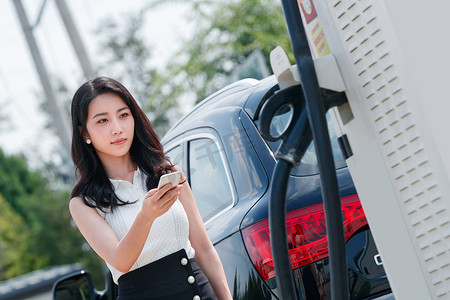 中国加油摄影照片_青年女人使用手机自助充电汽车