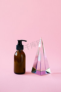 Bottle with pump for beauty product mockup and glass pyramid prism on pink background with copy space, vertical. Cosmetic product trendy minimalism