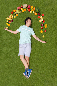 年轻男子躺在草地上手托着水果