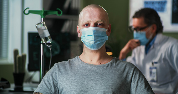 扛摄像机记者摄影照片_化疗期间戴口罩的秃头男子看着摄像机