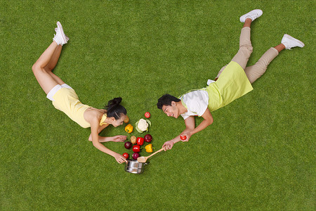 青年男女拿着蔬菜躺在草地上
