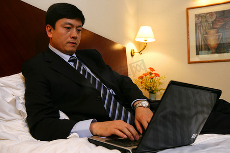 不舒服男摄影照片_商务人士在酒店床上使用笔记本电脑