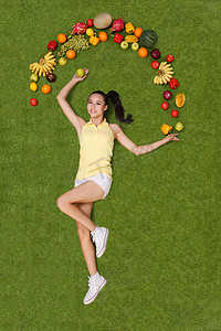 年轻女子躺在草地上手托着水果