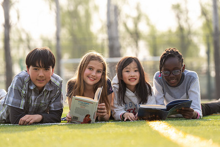 学生趴摄影照片_可爱的小学生们趴在草地上看书