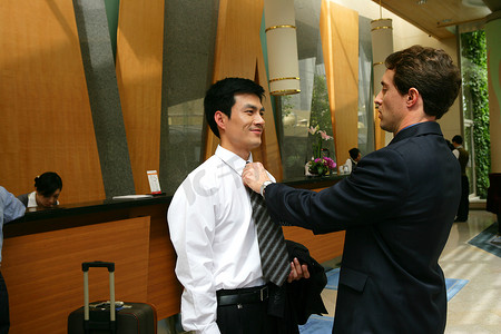 外国商务人士在酒店前台边为中国商务人士整理领带