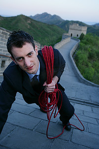 外国商务人士肩挎登山绳攀登长城