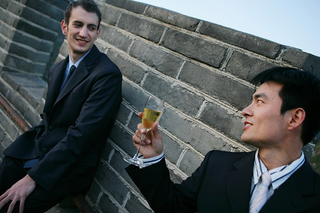 两位中外商务人士在长城上饮酒交谈