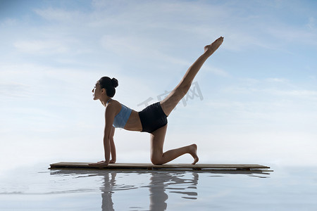 瑜伽动作摄影照片_年轻女人在水面上练习瑜伽