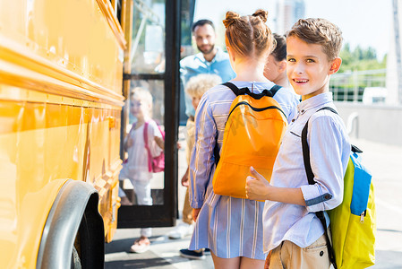 微笑的小男孩进入校车与同学, 而老师站在附近的门