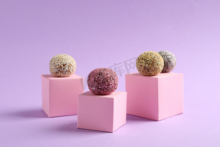 带有不同味道鲜美的素食糖果球和紫色背景粉红立方体的简约构图