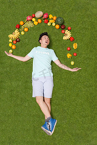 水果新鲜不新鲜摄影照片_年轻男子躺在草地上手托着水果
