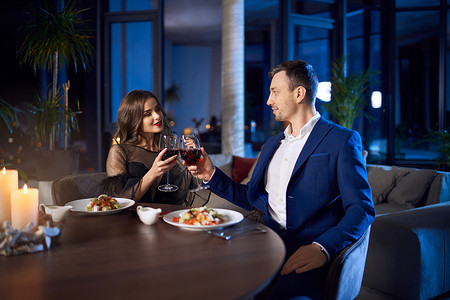 可爱的夫妻坐在餐桌旁，喝着葡萄酒和沙拉