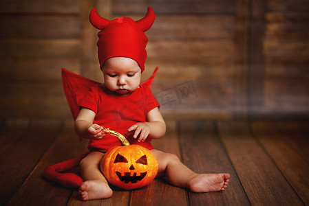有趣的婴儿在魔鬼万圣节服装与南瓜 