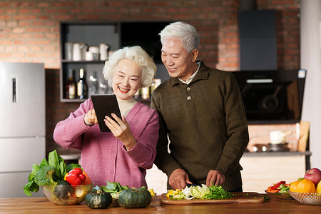 温馨美食摄影照片_做饭的老年夫妇使用平板电脑