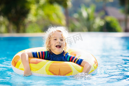 深入开展摄影照片_带充气玩具戒指的孩子漂浮在游泳池里。小男孩学习游泳和潜水在热带度假村的室外游泳池。和孩子们一起游泳。为儿童开展健康的体育活动。水的乐趣.