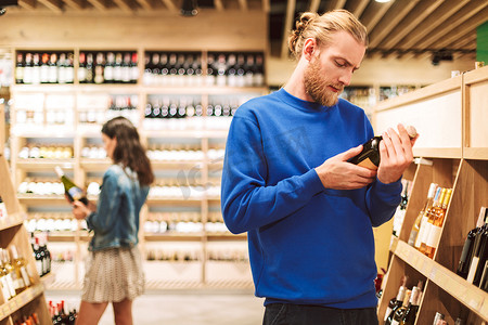 穿着深蓝色毛衣的年轻人若有所思地阅读现代超市的葡萄酒标签
