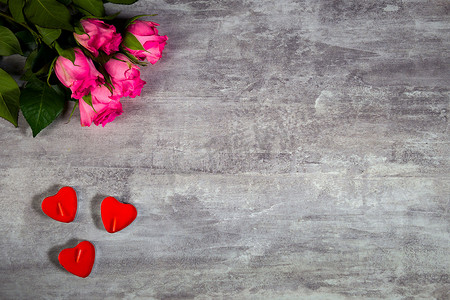 浪漫主题装饰摄影照片_粉色玫瑰和红蜡烛的密闭镜头，心形，躺在灰色的木制表面