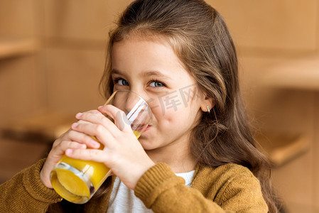 可爱的孩子喝橙汁在咖啡馆和看着相机