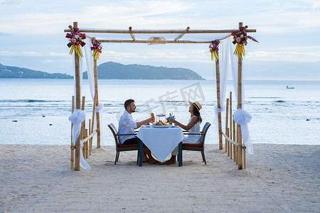浪漫晚餐摄影照片_泰国普吉海滩上的浪漫晚餐，日落时分，一对中年男子和一个欧洲男子在泰国海滩上共进晚餐