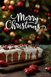 传统圣诞蛋糕的精选焦点，在圣诞花环附近的覆盆子放在木制桌子上，上面有快乐的圣诞插图