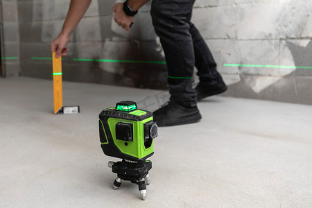 lines摄影照片_The worker inspector checks the floor level with a laser level meter that projects green lines on the cement walls in construction site.