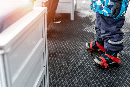 蓝色溜冰鞋摄影照片_在溜冰场更衣室里，穿着蓝色塑料租借溜冰鞋站在防滑橡胶软垫上的小孩腿的特写画面。健康儿童康乐活动