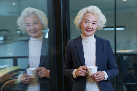 商务人士女士摄影照片_会议室内端着咖啡杯的商务老年女士