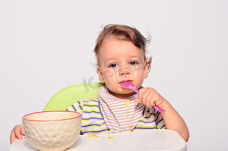 幼儿园ppt摄影照片_Baby eating food with a spoon, toddler eating messy and getting
