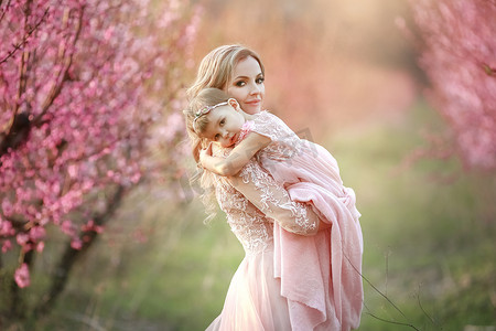 年轻美丽的母亲和她的小女儿的肖像。关闭仍然有爱心的家庭。迷人的女人抱着她的孩子在粉红色的花朵和微笑
