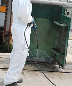 disinfestation with a pressure washer of street furniture during the coronavirus epidemic with the worker in white protective suit