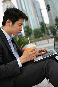 上海浦东写字楼旁一位男商务人士使用笔记本电脑时喝橙汁