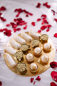糖果吧庆祝节日。生日或婚礼的甜自助餐。用玫瑰花瓣在金盘上的桌子上分发甜点