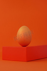创意几何色彩摄影照片_复活节彩蛋在几何形状讲台上的橙色背景.褐色鸡蛋平衡基座等距简约。创意最小的时髦单色色彩依旧生机勃勃.现代构成.