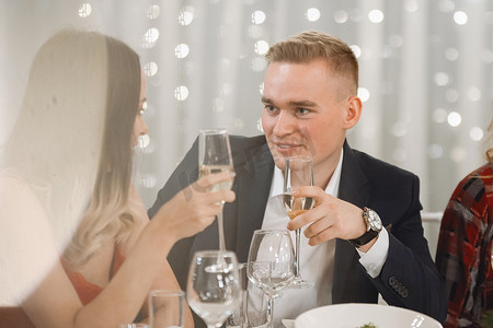一对年轻夫妇坐在节日桌上，喝着香槟酒，面带微笑，在餐馆里聊天。有选择的焦点，模糊的灯光.