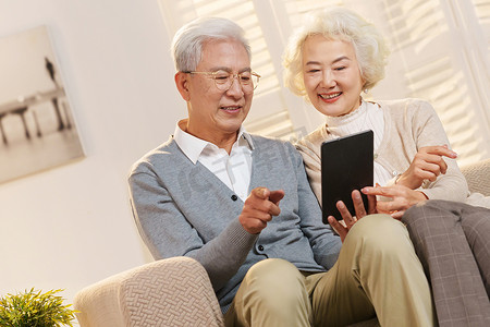 永远年轻摄影照片_老年夫妇坐在沙发上使用平板电脑