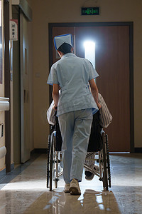 老人坐轮椅摄影照片_走廊内护士推坐轮椅的老人背影