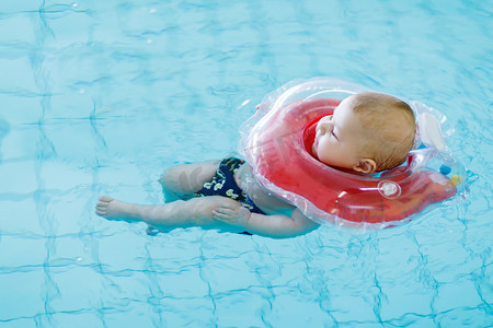 可爱的小婴儿学习与在室内游泳池游泳圈游泳