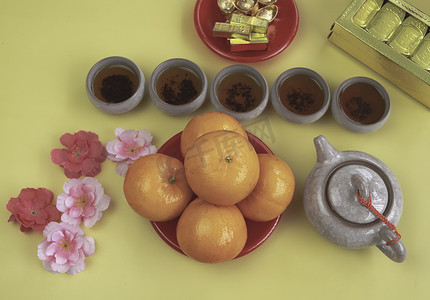 红色菜色的橙子和五个茶杯放在模糊的金色缩影前，背景上写着中文吉祥的字样
