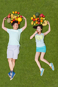 青年男女拿着水果躺在草地上