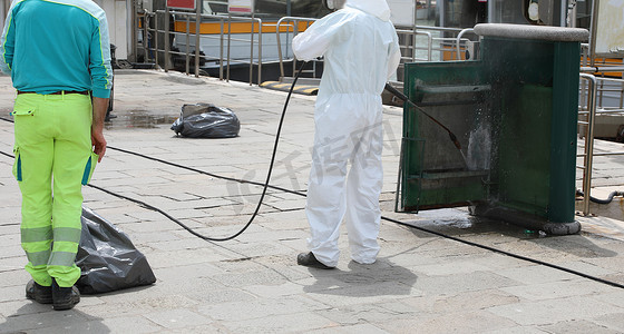 disinfestation of street furniture during the coronavirus epidemic with the worker in protective white overalls