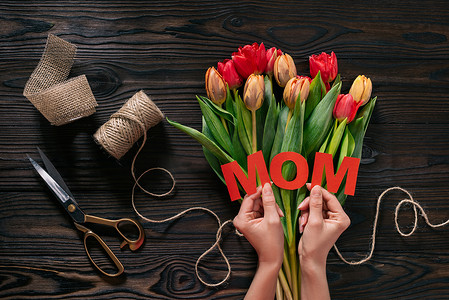 母亲的部分看法在手和郁金香在木桌上的花束, 母亲节概念的妇女