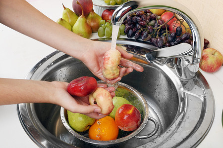 在滤器放在水槽里洗桃和其它水果的女人的手