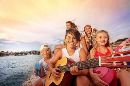 年轻朋友的肖像, 快乐的十几岁的男孩和女孩, 在海边弹吉他